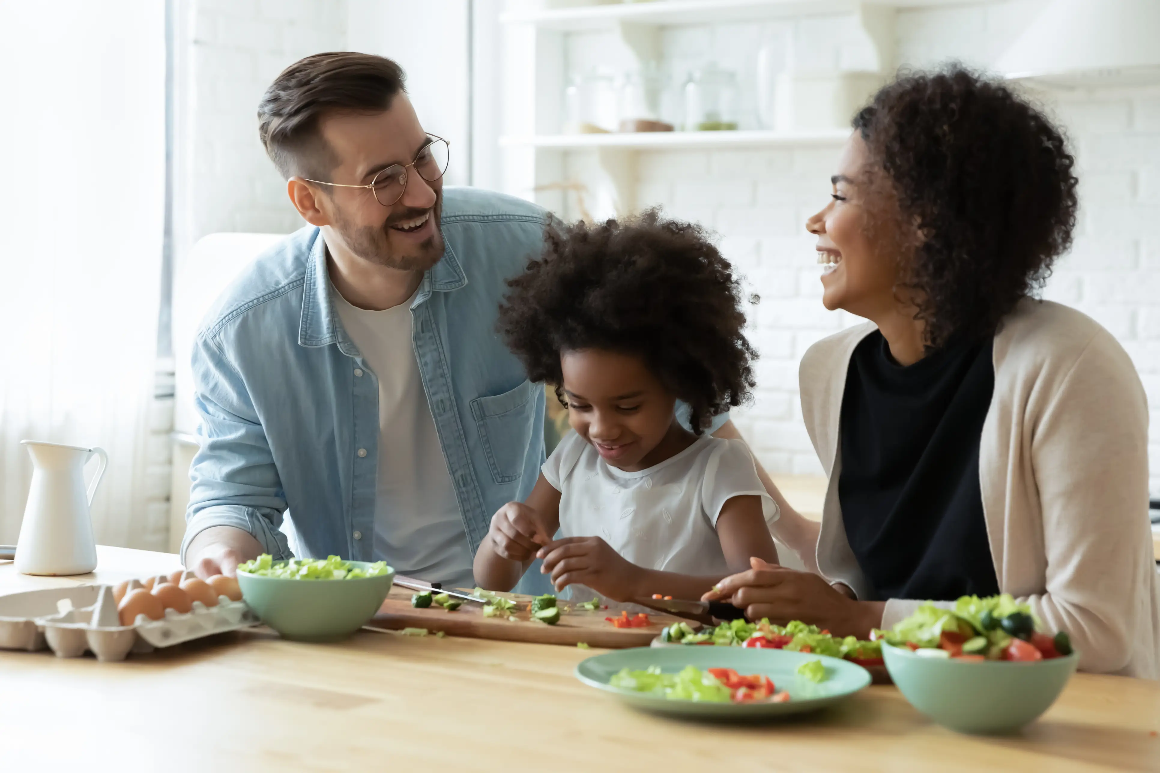 a man and woman smiling while a girl is cutting vegetables