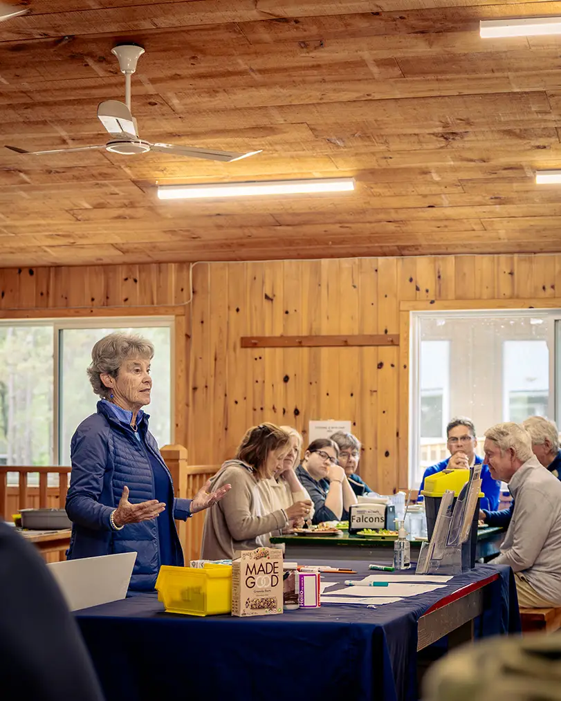 a woman standing in front of a table with people sitting at tables