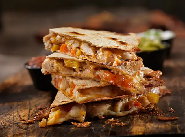 a stack of quesadilla with a bowl of salsa