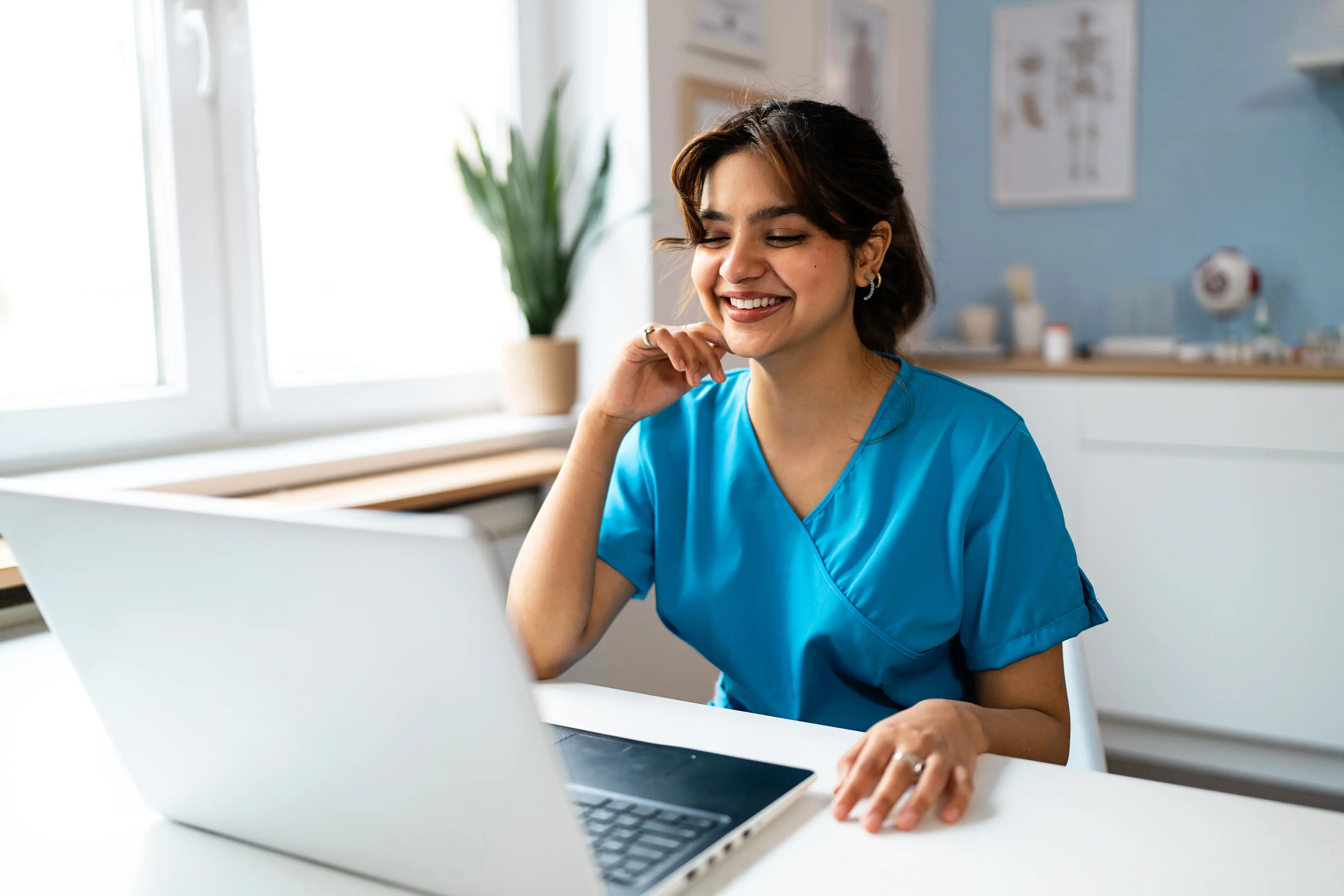 a woman in blue scrubs sitting at a desk with a laptop