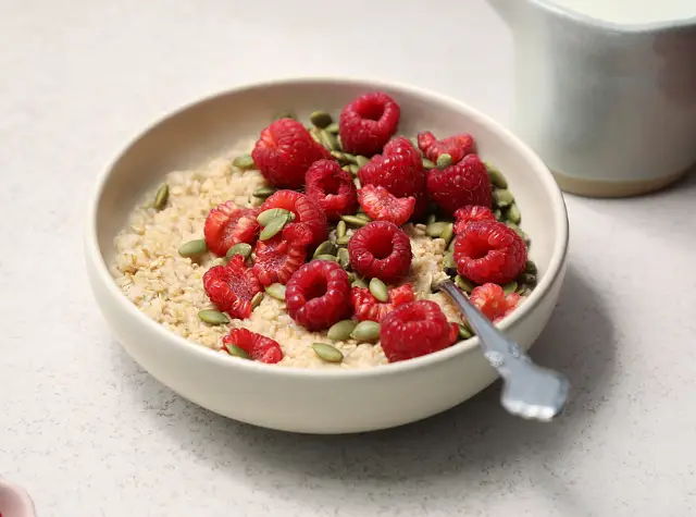 a bowl of oatmeal with raspberries and seeds